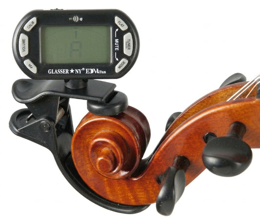 A digital violin tuner clip mounted on a violin's scroll, showing a black display screen with a green backlight and control buttons, set against a plain white background.